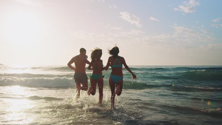 A group of friends, two girls and a boy, having fun at the ocean. They standing in the water and splashing around.