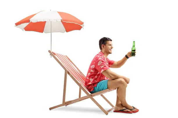 Photo of Tourist with a bottle of beer sitting in deck chair with an umbrella