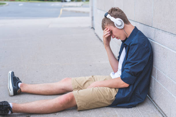 Upset teen sitting on the ground against a wall while listening to music. stock photo