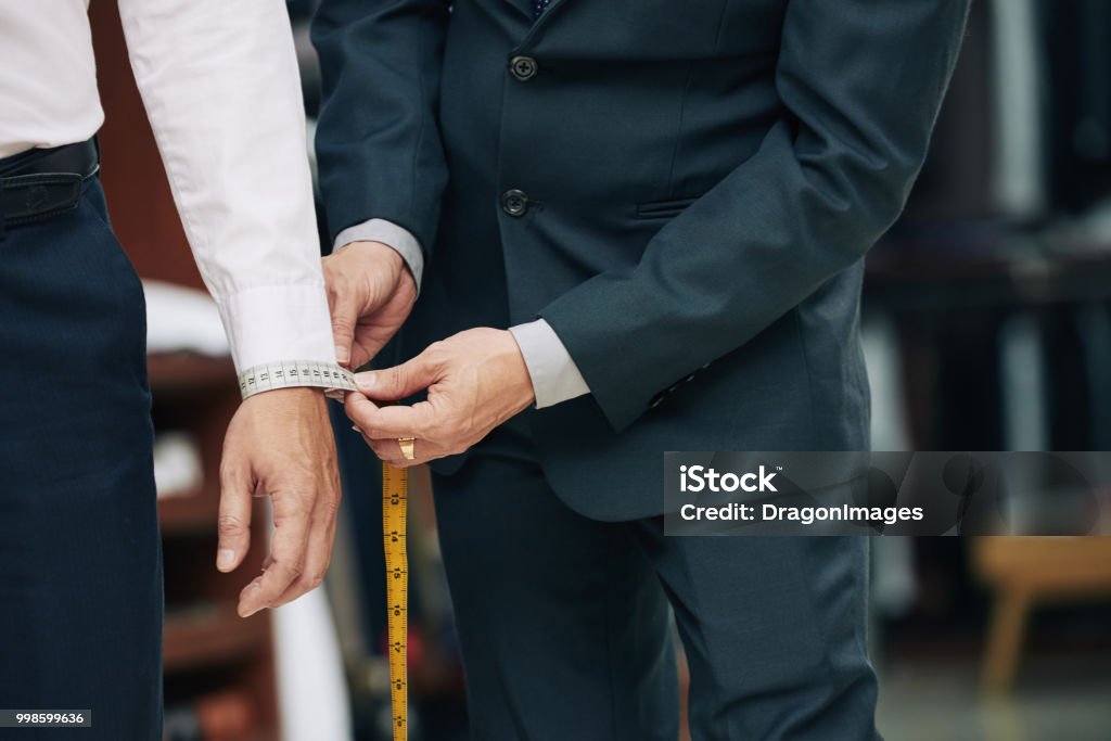 Measuring cuff Cropped image of tailor measuring cuff of male client Tailor Stock Photo