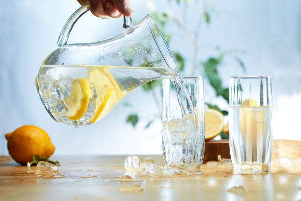 Water from a Decanter with sliced lemon, ice poured into a glass. stock photo