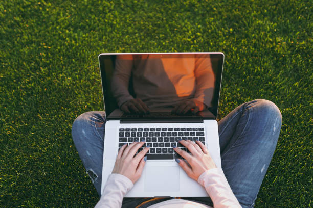 istock Overhead top view hands on keyboard. Woman working on laptop pc computer with blank black empty screen to copy space on green grass sunshine lawn outdoors. Mobile Office. Freelance business concept. 998660116