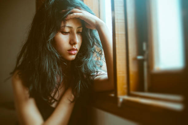 Smutna młoda kobieta myśli w pobliżu okna. – zdjęcie
