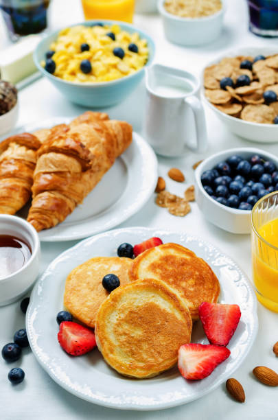 istock Breakfast table setting with flakes, juice, croissants, pancakes and fresh berries 998675204