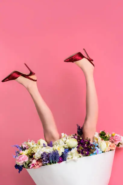 Photo of cropped shot of girl in high heeled shoes and skirt with beautiful flowers on pink, upside down view