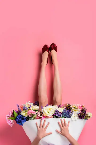 Photo of upside down of girl in high heeled shoes and skirt with beautiful flowers isolated on pink