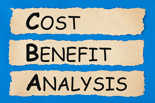 Cost-Benefit Analysis (CBA) written on old torn paper on blue background. Business concept.
