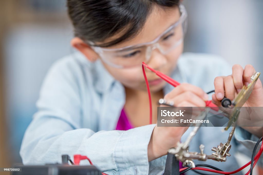 Working with circuits An asian elementary school girl is doing a science experiment at home. She is wearing googles for safety while testing the voltage of a circuit. Brown Hair Stock Photo