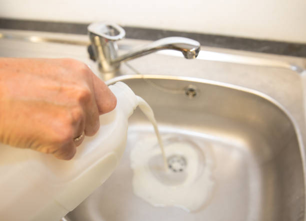 Fresh milk being poured down a stainless steel sink, waste stock photo