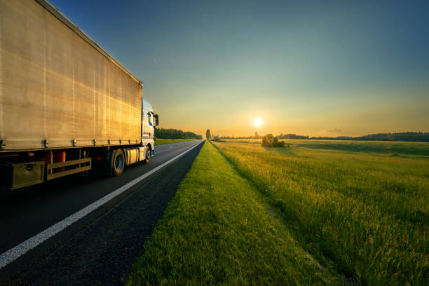 黄金の夕日の農村景観におけるアスファルト道路上の運転トラック - distant field meadow landscape ストックフォトと画像