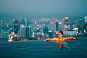Young woman relaxing in the pool as the sun sets above Kuala Lumpur