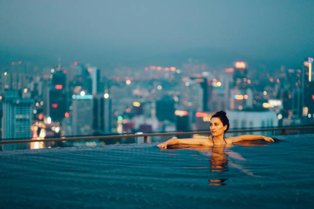 Young woman relaxing in the pool as the sun sets above Kuala Lumpur Young brunette woman relaxing in the pool, swimming on top of the building in Kuala Lumpur, Malaysia. She is having a moment to relax after work in the busy city of Kuala Lumpur, Malaysia. exclusive travel stock pictures, royalty-free photos & images