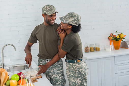 Woman and man in army uniform hugging in kitchen
