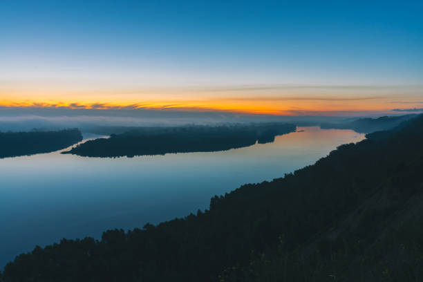 istock View from high shore on broad river. Riverbank with forest under thick fog. Dawn reflected in water. Yellow glow in picturesque predawn sky. Colorful morning atmospheric landscape of majestic nature. 998848146