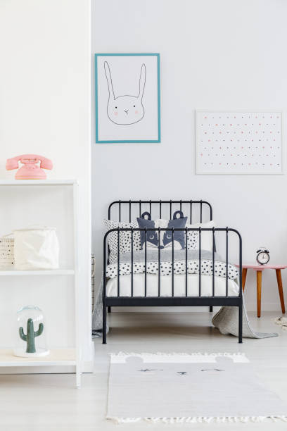 istock Child's bed with black metal frame in a small, simple bedroom interior. Rabbit poster on a white wall. Real photo 998848266