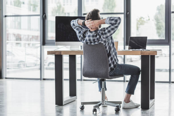 istock back view of young programmer sitting with hands behind head at workplace 998848664