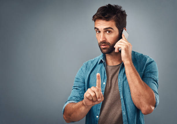 Please hold while I tale this call Studio shot of a handsome young man using a mobile phone against a grey background Gesturing stock pictures, royalty-free photos & images