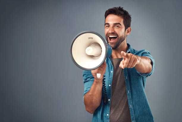 You're our winner of the day! Studio shot of a handsome young man using a megaphone against a grey background content marketing stock pictures, royalty-free photos & images