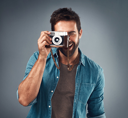 Studio shot of a handsome young man using a camera against a grey background