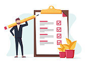 istock Positive business man with a giant pencil on his shoulder nearby marked checklist on a clipboard paper. 998854988