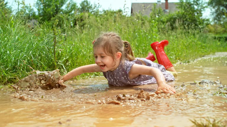 SLO MO Little girl lying in a puddle and moving her hands as if she were swimming