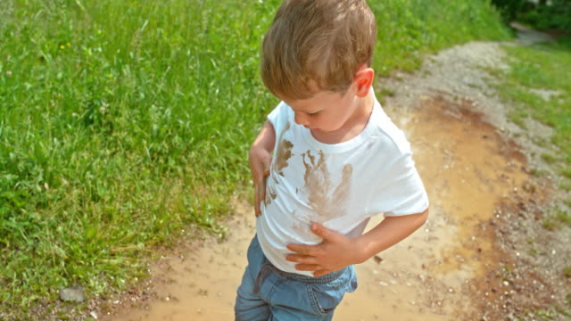 SLO MO Little boy putting his hands in the muddy puddle and wiping them in his clean white t shirt