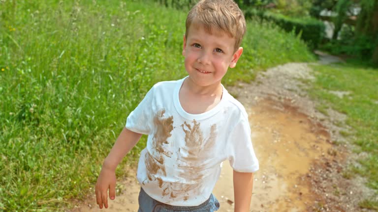 SLO MO Little boy standing in the puddle with a dirty white t shirt smiling into the camera