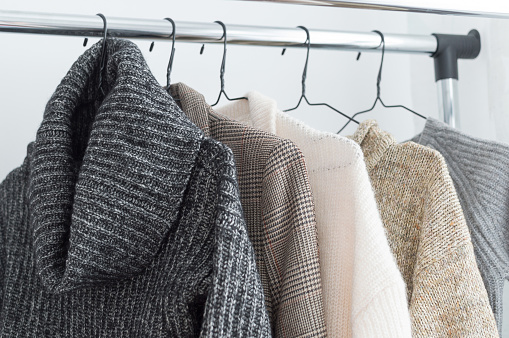 Winter wardrobe showcase. White and gray tone knitwear hanging on a clothes rack. Selective focus, horizontal