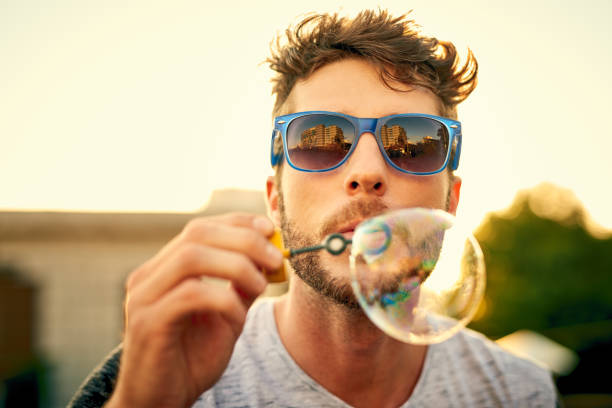 Our inner child never really leaves us Shot of a young man blowing bubbles outdoors never stock pictures, royalty-free photos & images