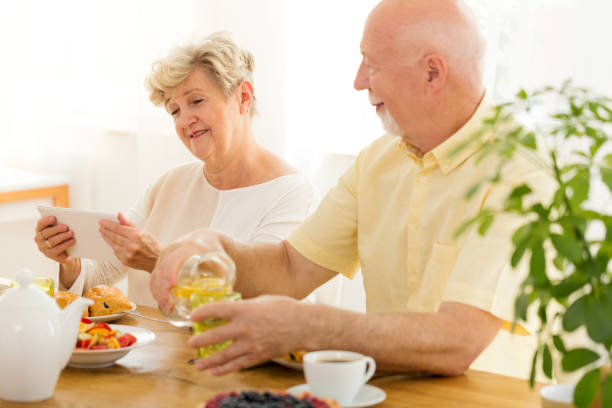 istock Senior woman using tablet while grandfather drinking water during breakfast 998982920