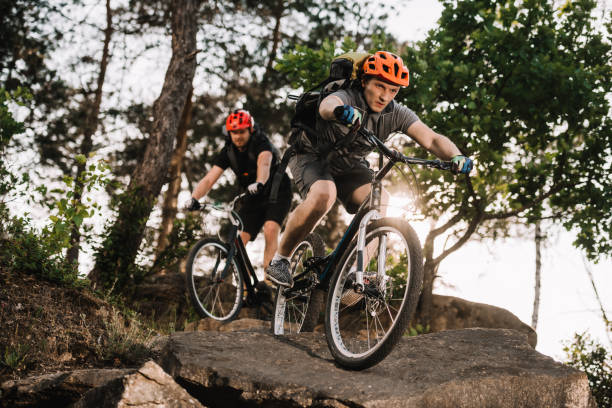 istock athletic young trial bikers riding on rocks at pine forest 998984030