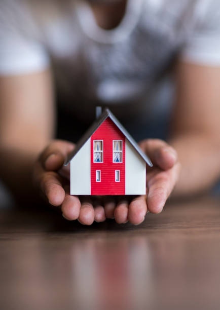 Old man protecting house model with hands.Risk insurance.The concept of mortgages and Bank loans. Poverty. Rental property.