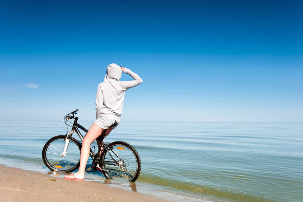 istock Young sporty lady resting from riding bicycle on the beach 998997810