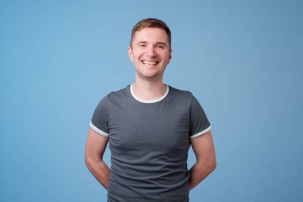 istock Confident young handsome man keeping arms crossed and smiling while standing against blue white background 999008906