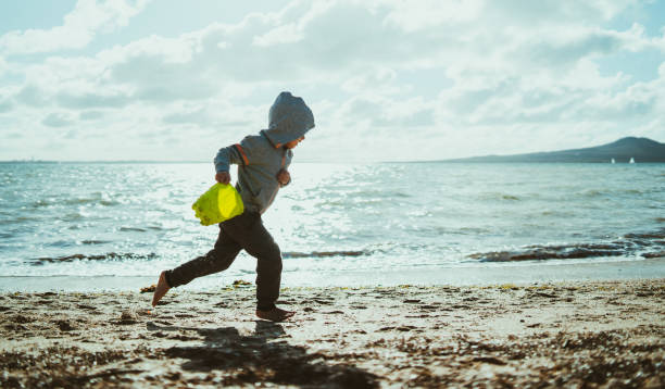 Having fun running at beach in winter. Kid holding bucket in his hand and running at beach in Auckland, new Zealand. rangitoto island stock pictures, royalty-free photos & images