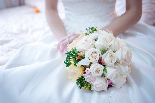 Image of bride holding beautiful bouquet while sitting on bed at home