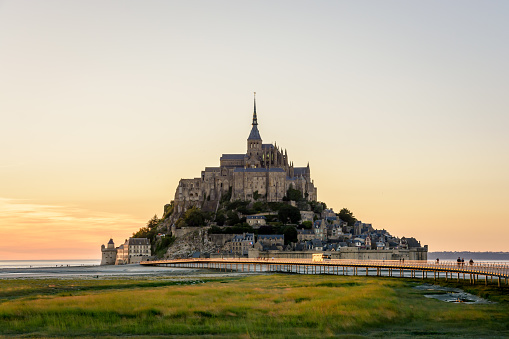 Le Mont-Saint-Michel, France - June 25, 2018: View of the Mont Saint-Michel tidal island at sunset with a shuttle bus driving on the jetty on stilts open in 2014 as part of the bay dredging program.