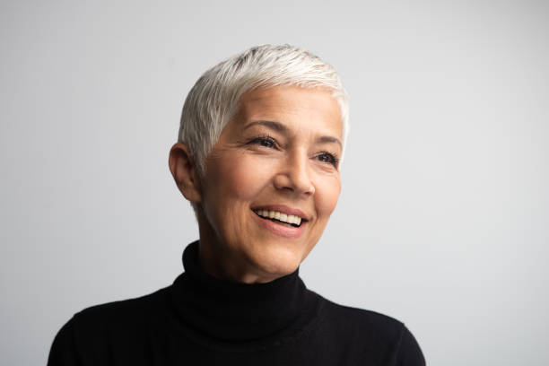 Beautiful 50+ woman posing in studio in front of grey background.