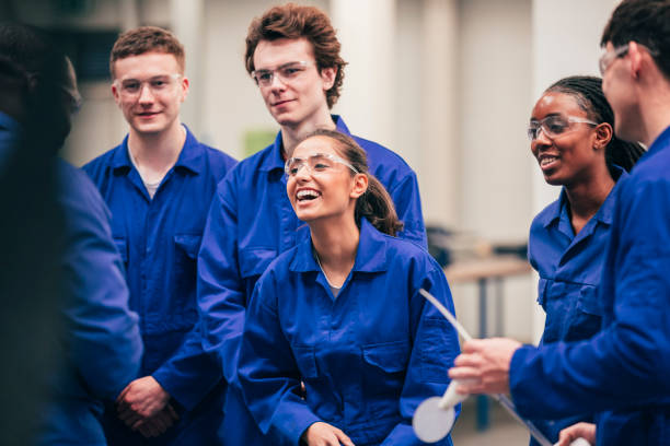 Enjoying Engineering Class A young Indian woman, who is wearing protective eyewear, smiles as she enjoys her engineering class with her peers - they are all wearing blue coveralls. trainee stock pictures, royalty-free photos & images