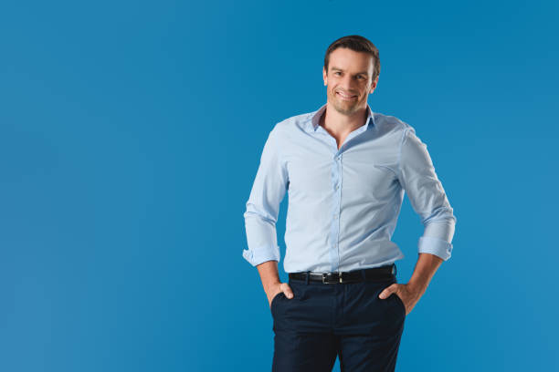 istock handsome man standing with hands in pockets and smiling at camera isolated on blue 999094008
