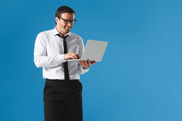 istock smiling handsome businessman in eyeglasses using laptop isolated on blue 999094168