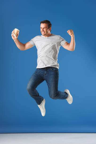 istock excited man with coffee to go jumping and triumphing on blue 999096872
