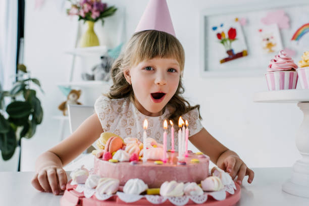 istock smiling kid in cone blowing out candles from birthday cake 999098222