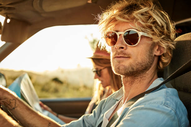 Man wearing sunglasses by woman in van Handsome mid adult man wearing sunglasses by girlfriend in van during sunset. Confident male is driving while female is reading map during road trip. He is having blond hair. hipster car stock pictures, royalty-free photos & images