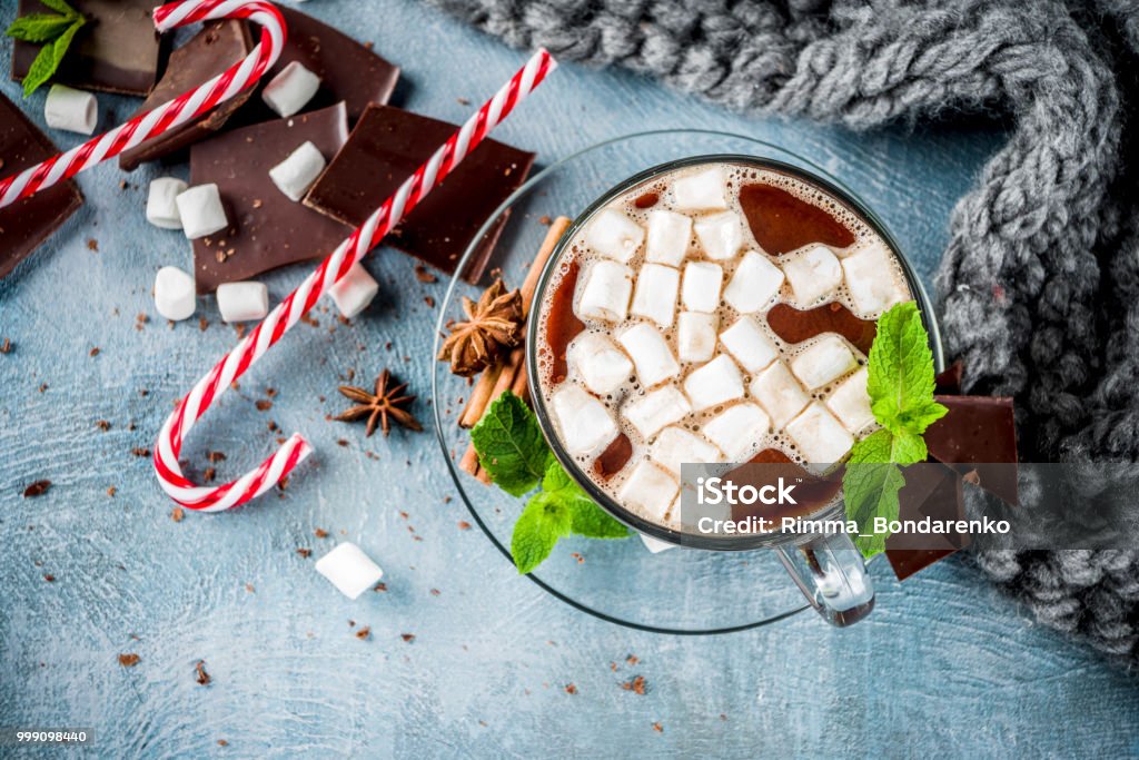 Hot chocolate with mint and marshmallow Homemade hot chocolate with mint, candy cane and marshmallow, light blue background with warm blanket, copy space Anise Stock Photo