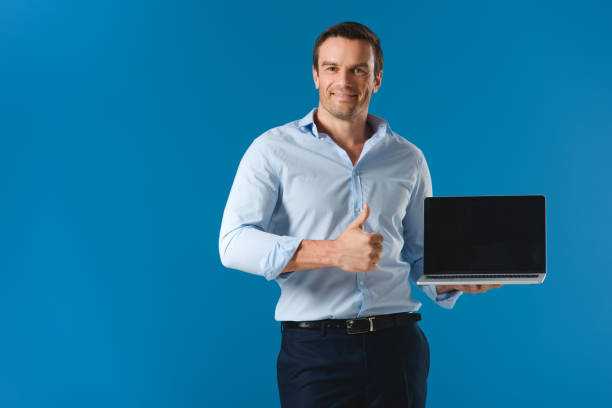 istock handsome man holding laptop with blank screen, showing thumb up and smiling at camera isolated on blue 999098718