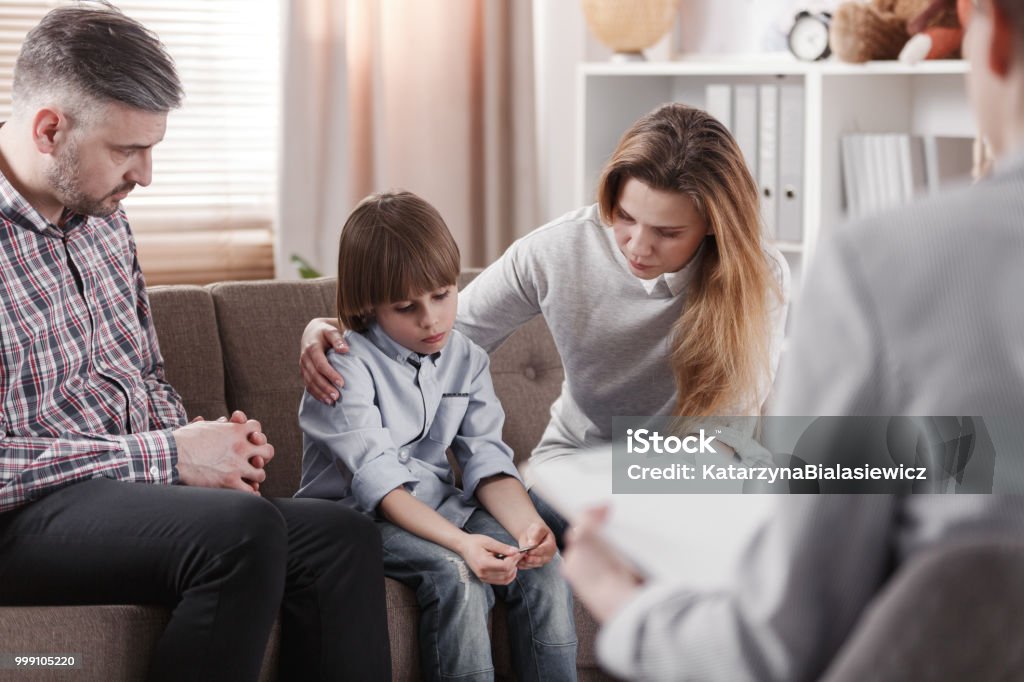 Mother hugging her autistic son, sitting next to a father during a family therapy Family Stock Photo