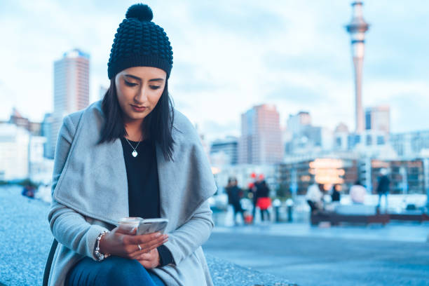 vérification des médias sociaux sur téléphone avec la ville d’auckland en arrière-plan. - winter migration photos et images de collection