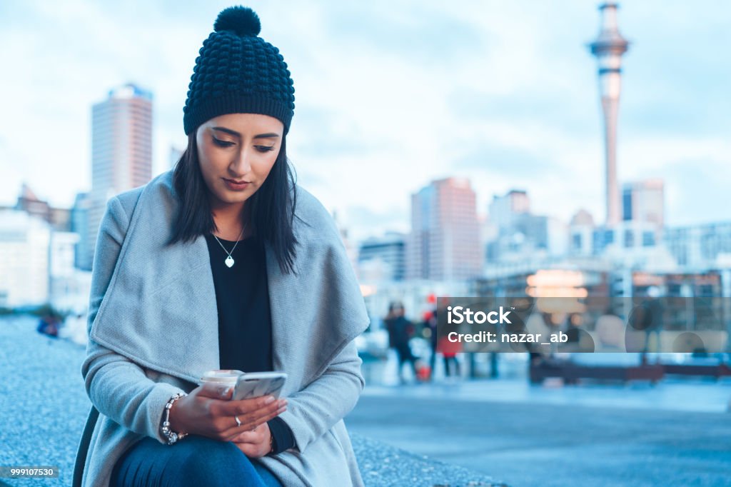 Checking social media on phone with Auckland city in background. New Zealand Stock Photo