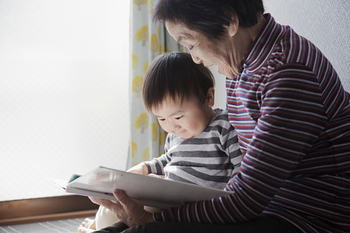 Japanese senior woman and her grandson reading a picture book at home.